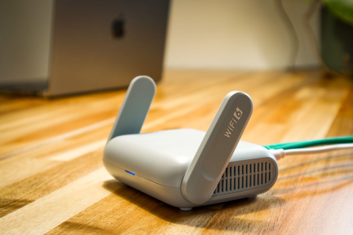 Biały router Wi-Fi na drewnianym biurku obok laptopa